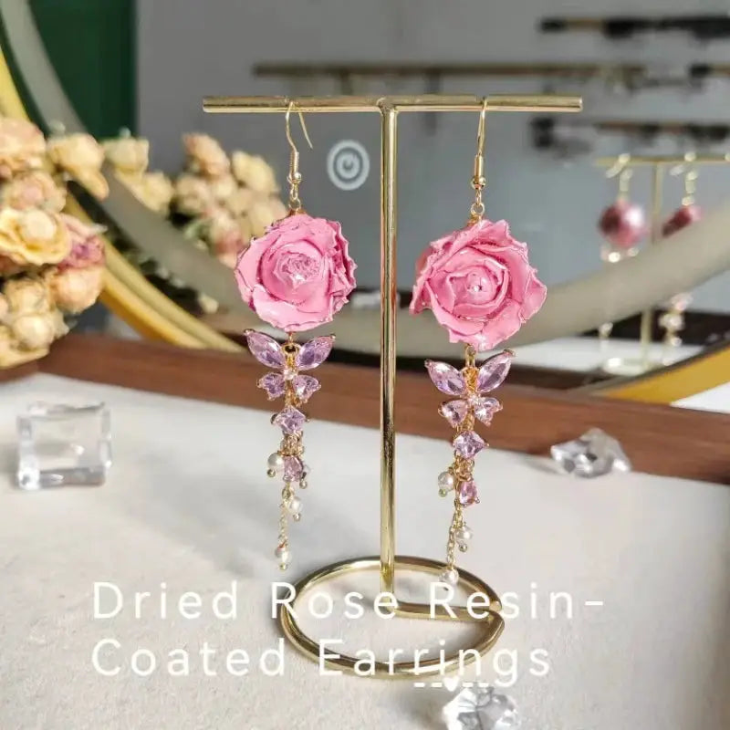 Pair of Simples Market Elegant Immortal Rose long earrings with pink epoxy resin roses and dangling purple crystals.