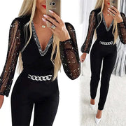 Women's black jumpsuit with sheer dotted sleeves, V-neck rhinestone trim, and chain belt.