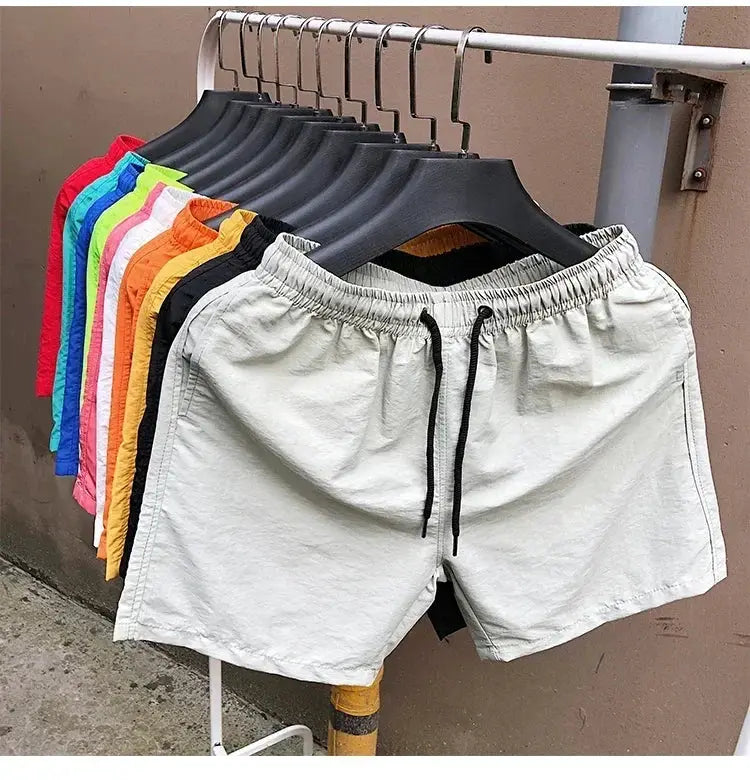 Simples Market men's swim shorts, 2024 summer collection; front grey drawstring pair with a multicolor lineup behind.