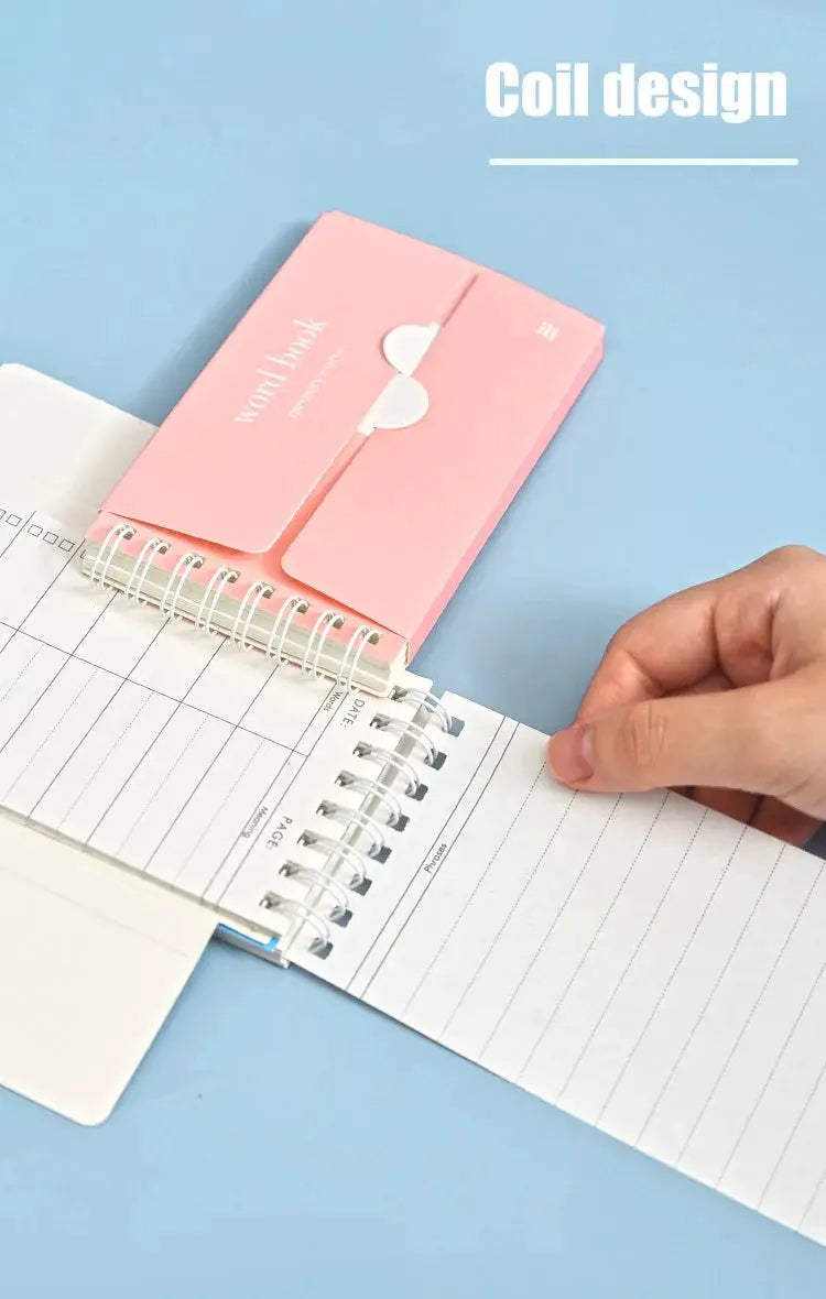 Pink word-book notebook with coil binding beside a white spiral-bound planner; school office supplies