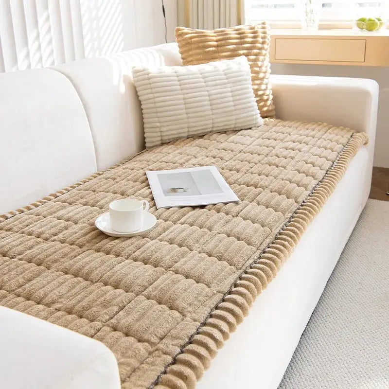 Thicken Quilting Warm Stripe Flannel Sofa Pad beige on white sofa, quilted stripe design with magazine and cup.