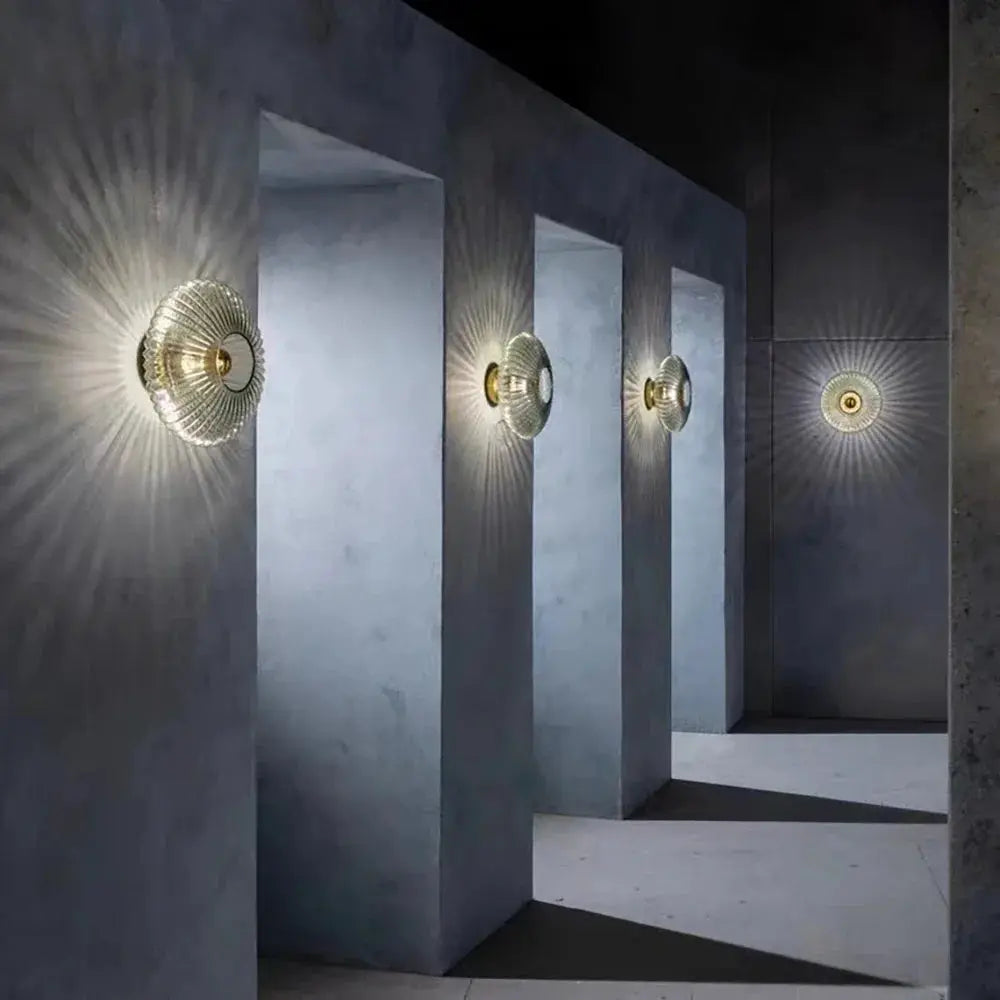 Four Nordic LED glass wall sconces with ribbed circular shades and gold mounts line a blue hallway.
