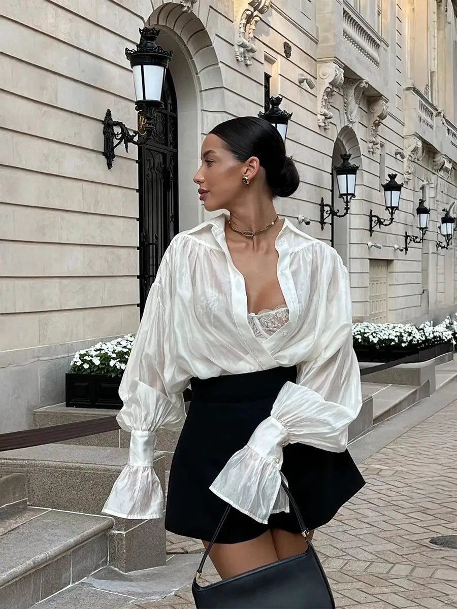 Loose collared white blouse with dramatic flare sleeves and lace detail, paired with a black mini skirt.