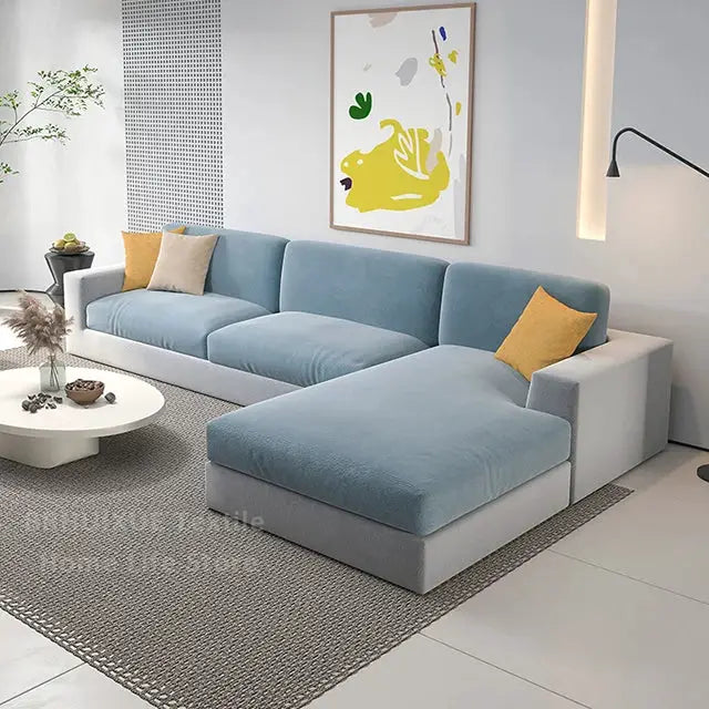 Velvet L-shaped sectional sofa by Simples Market with light blue cushions, yellow throw pillows, and grey base