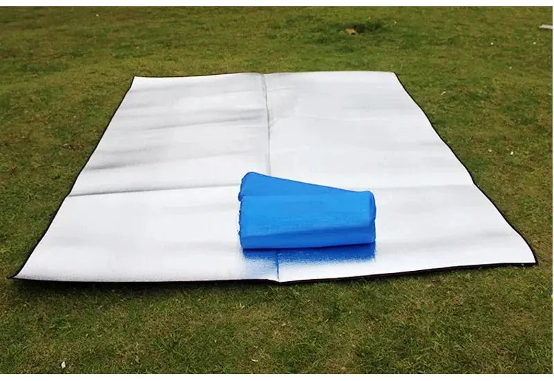 Two camping mats on grass: aluminum foil insulated mat and blue foam sleeping pad
