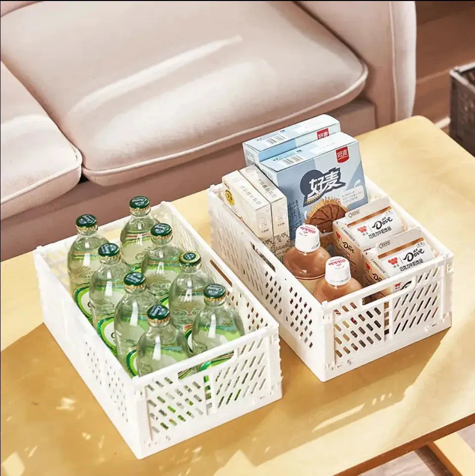 Two white plastic foldable storage crates on a table; left crate with bottled drinks, right with boxes.