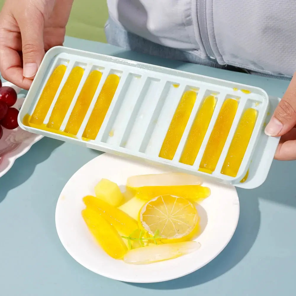 Long-bar ice cube mold with yellow juice-filled ice sticks, held above a white plate with lemon slices.
