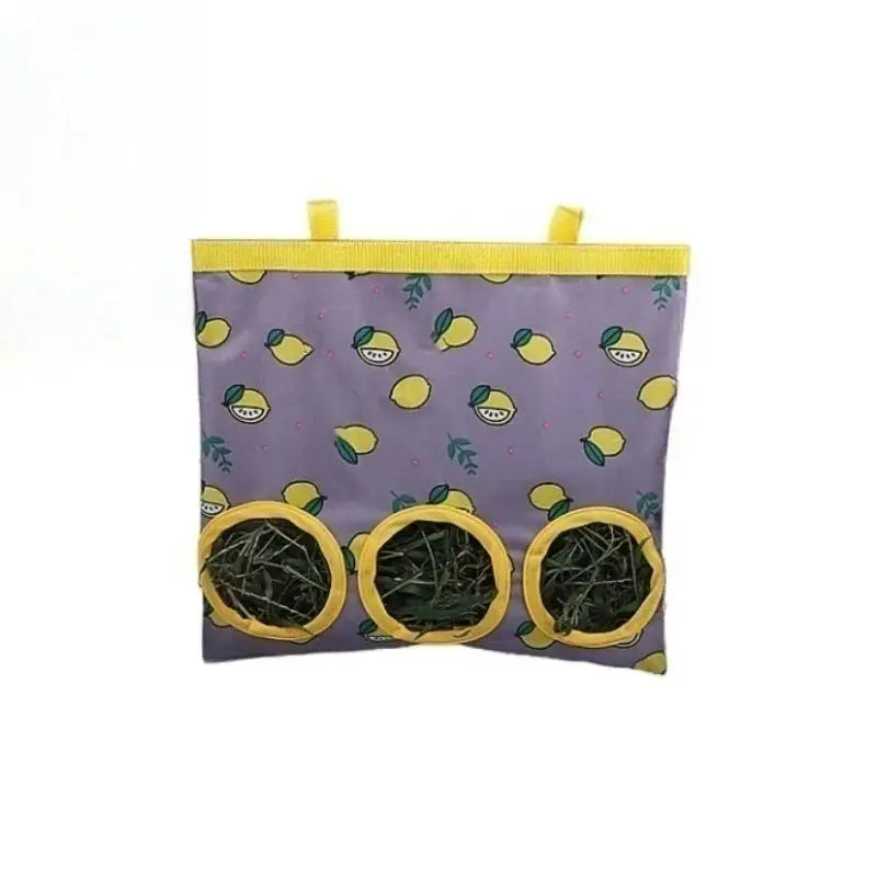Rabbit hay bag hanging feeder with 3 yellow-rimmed openings on purple lemon-pattern fabric, filled with hay.
