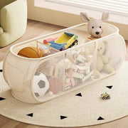 Portable white mesh toy organizer with handles by Simples Market, filled with plush toys, a toy truck, and a ball.