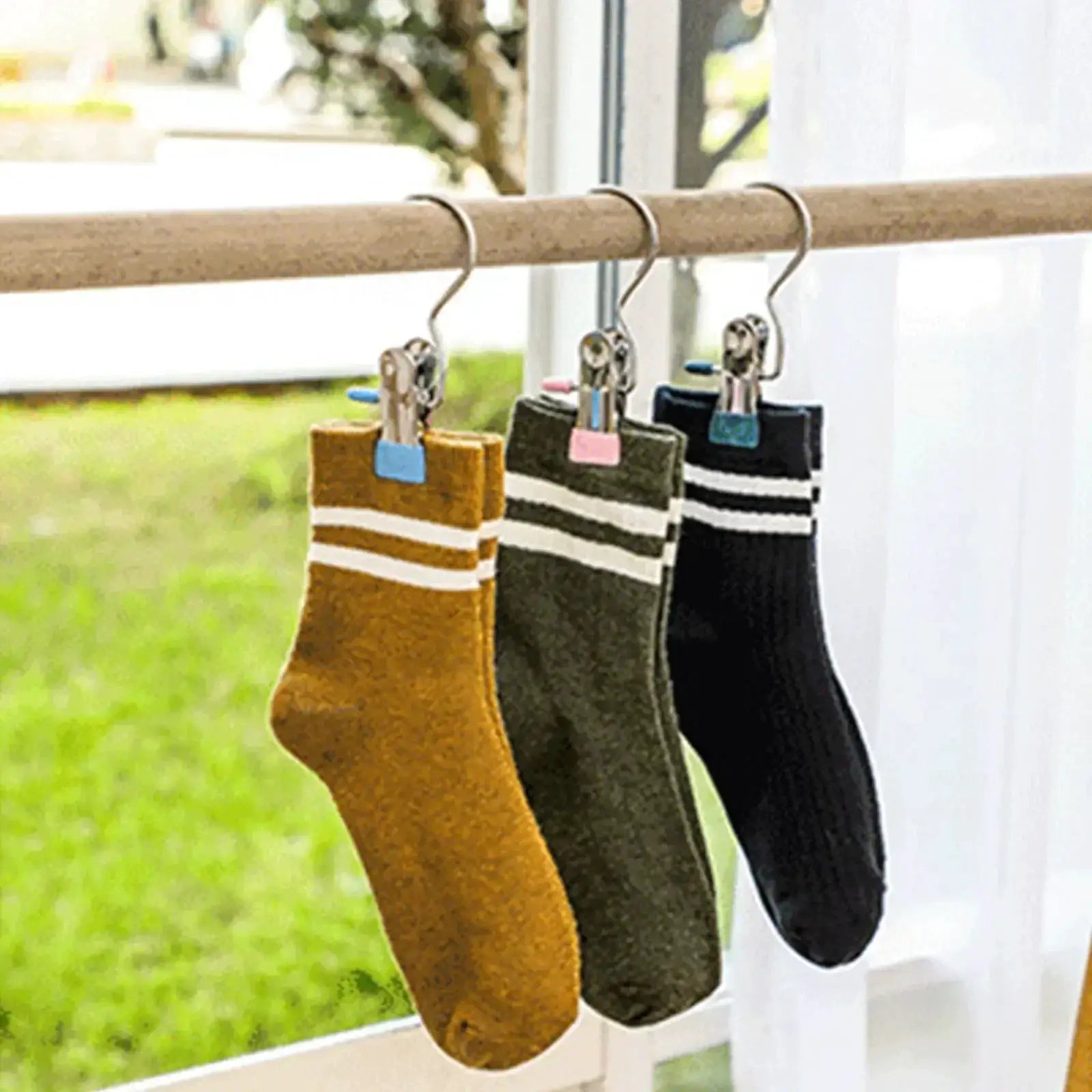 Stainless steel clothespins on a wooden rod clipping 3 socks (brown, olive, black) by a window