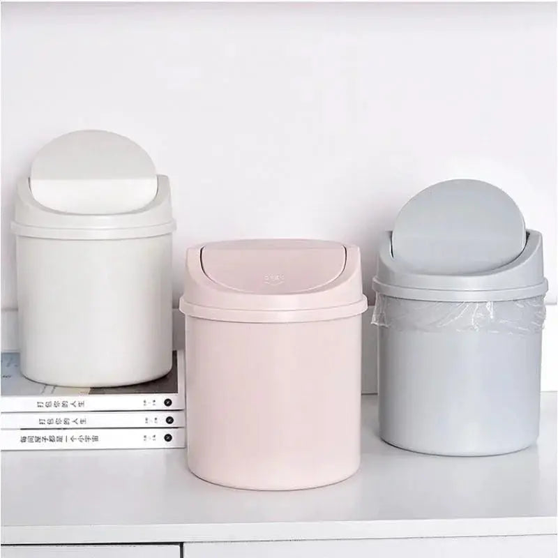 Three mini desktop trash cans with lids in white, pink, and gray plastic by Simples Market