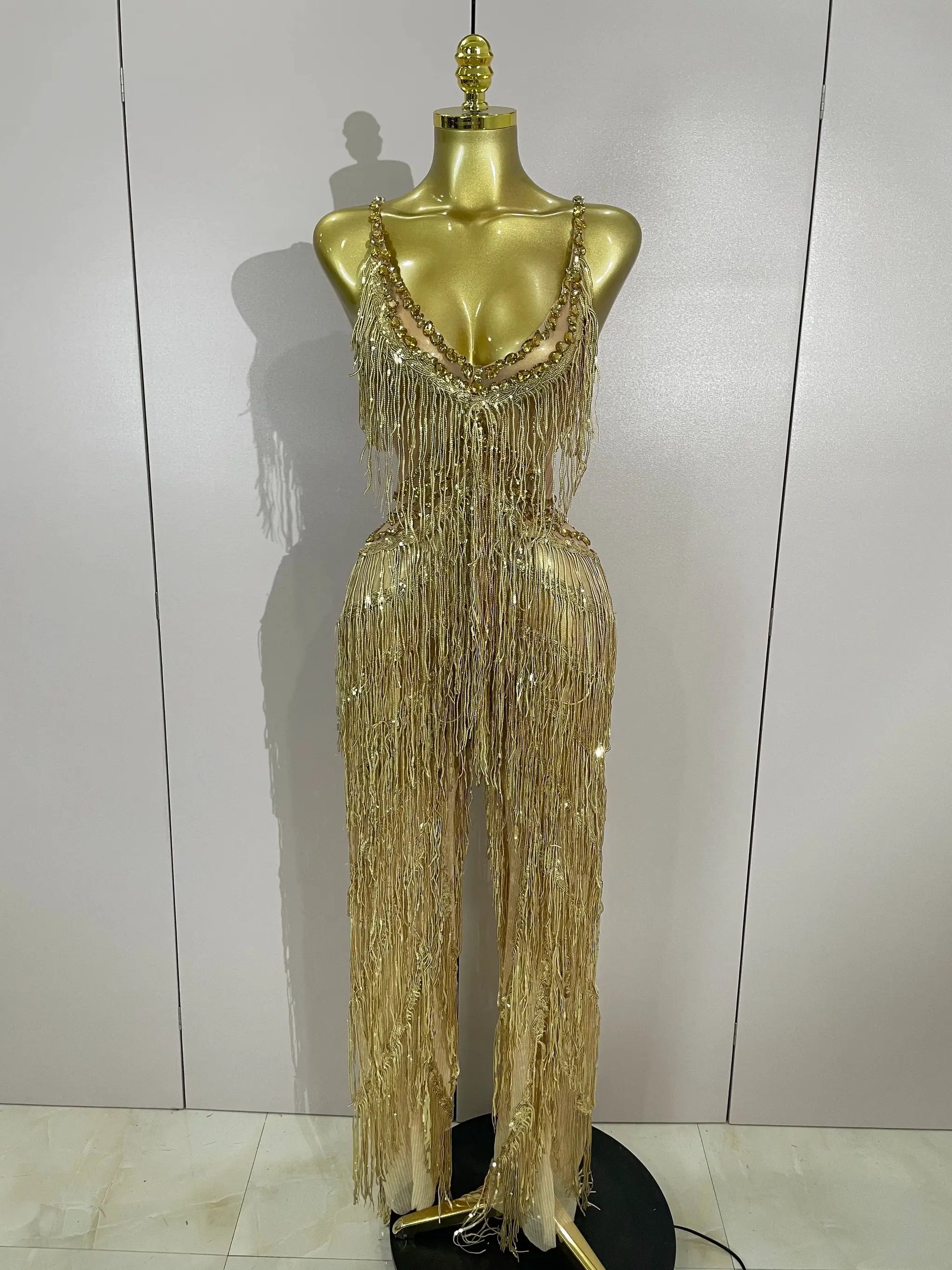 Gold sequined fringe jumpsuit with rhinestone straps on display mannequin