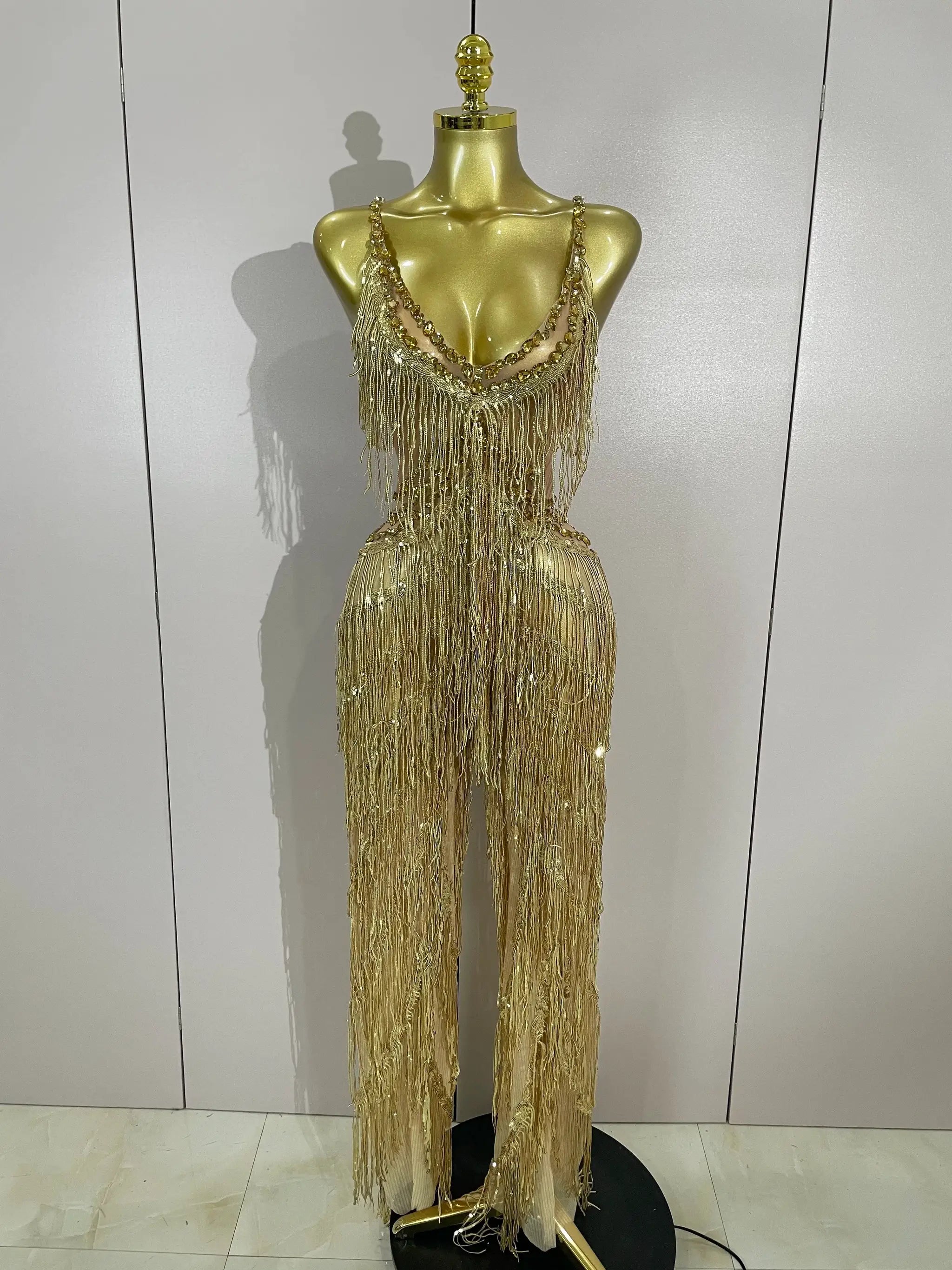 Gold sequined fringe jumpsuit with rhinestone straps on display mannequin