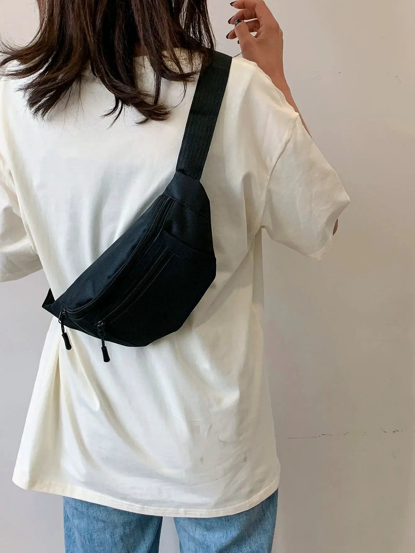 Black crossbody fanny pack with zip pockets worn over a white shirt