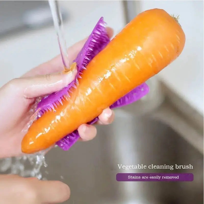 Silicone vegetable cleaning brush by Simples Market with purple bristles cleaning a carrot under running water