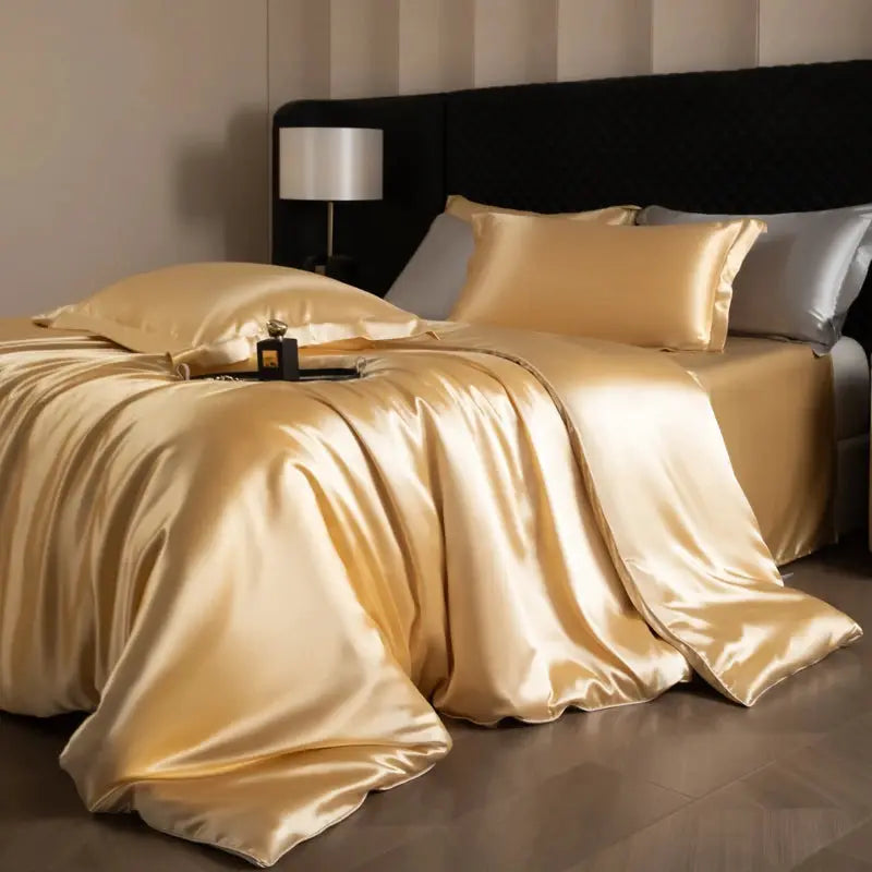 Silk bed sheets set in gold satin on a bed with duvet cover, fitted and flat sheets, and pillowcases.