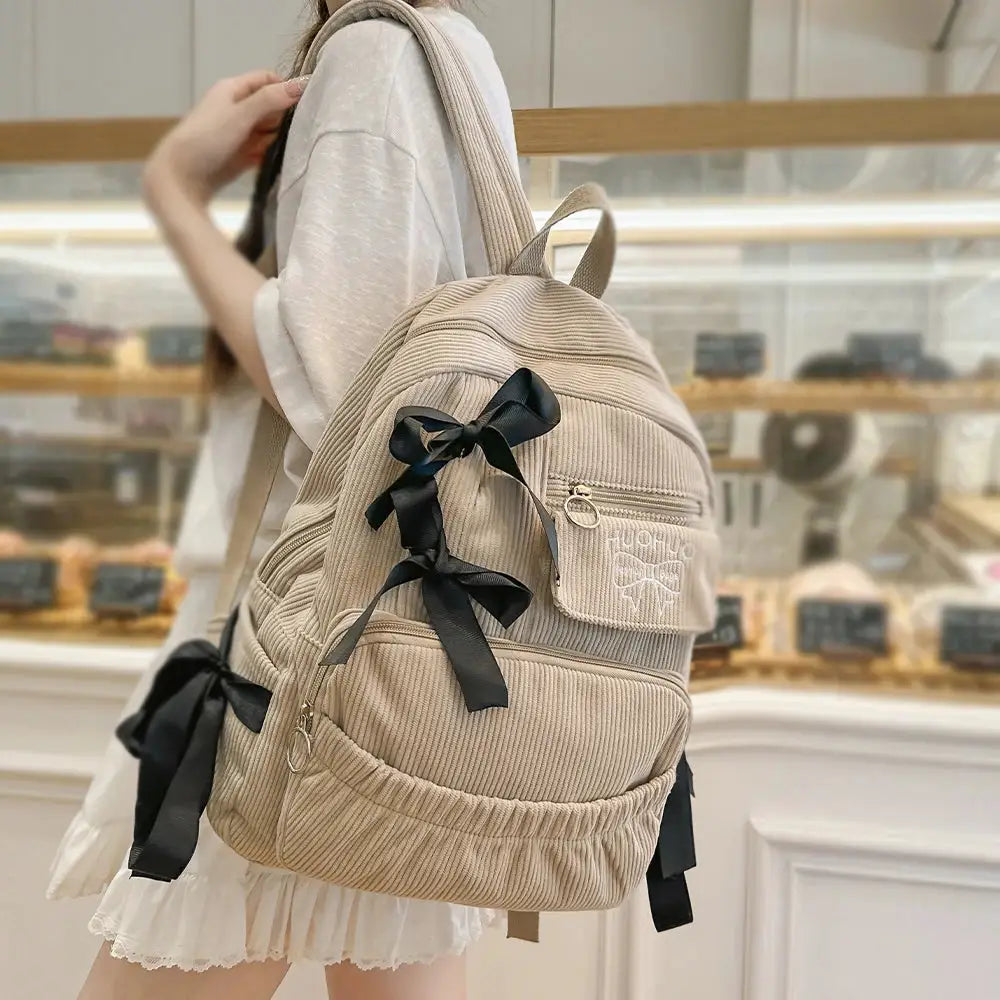 Backpack beige corduroy with black ribbon bows on straps and front pocket, multiple zip pockets
