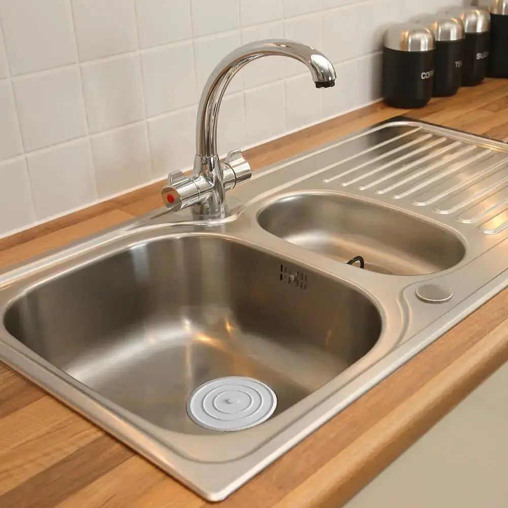 Large silicone drain stopper by Simples Market in a double-basin stainless steel kitchen sink; round flat cover