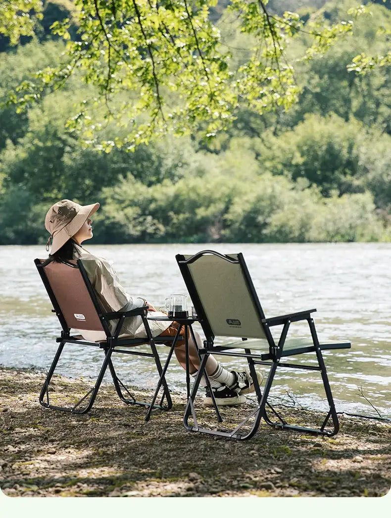Two BISINNA outdoor folding camping chairs by Simples Market, beige and olive seats by the lakeside.