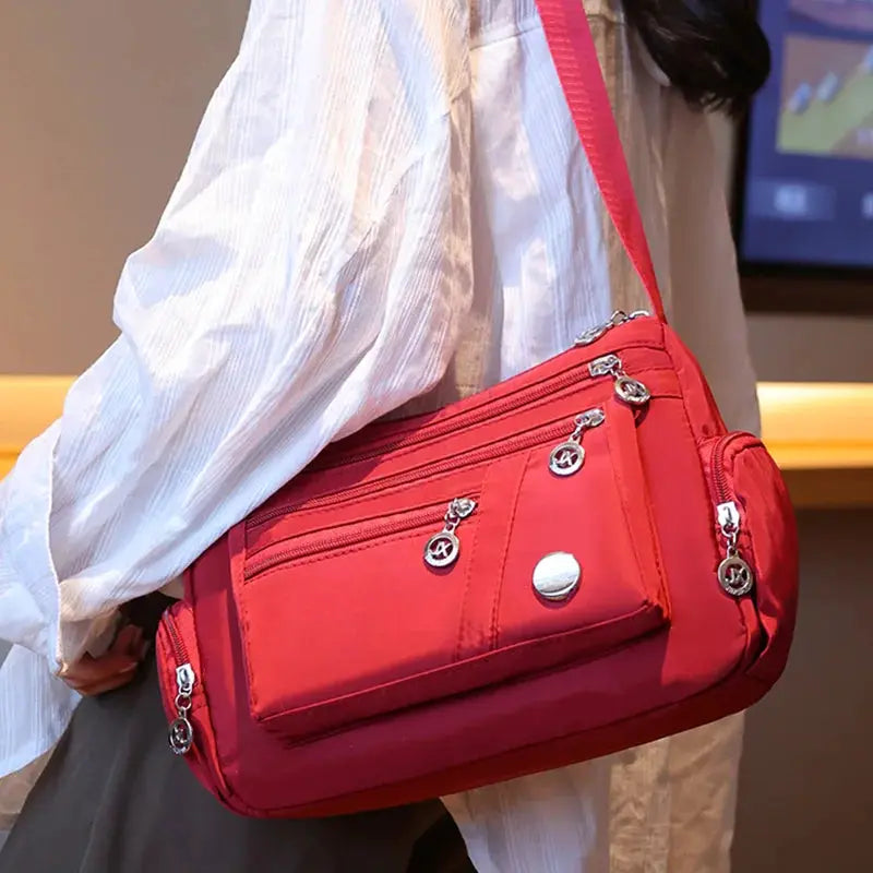 Ladies' red nylon crossbody handbag with multiple zip pockets and an adjustable shoulder strap