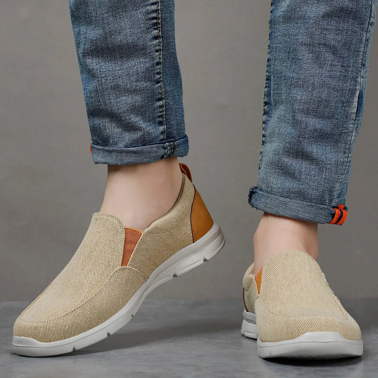 Pair of men's beige canvas slip-on sneakers with white sole and orange heel accents