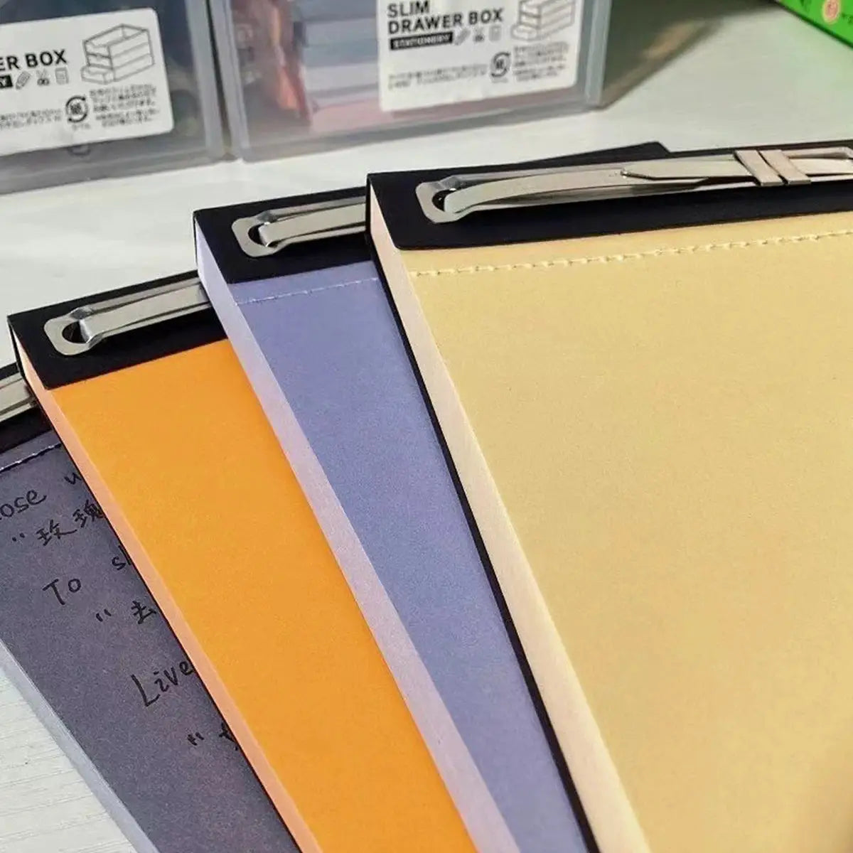Simples Market Plande notebooks; four pocket notepads with orange, purple, blue, and beige covers, metal top clips