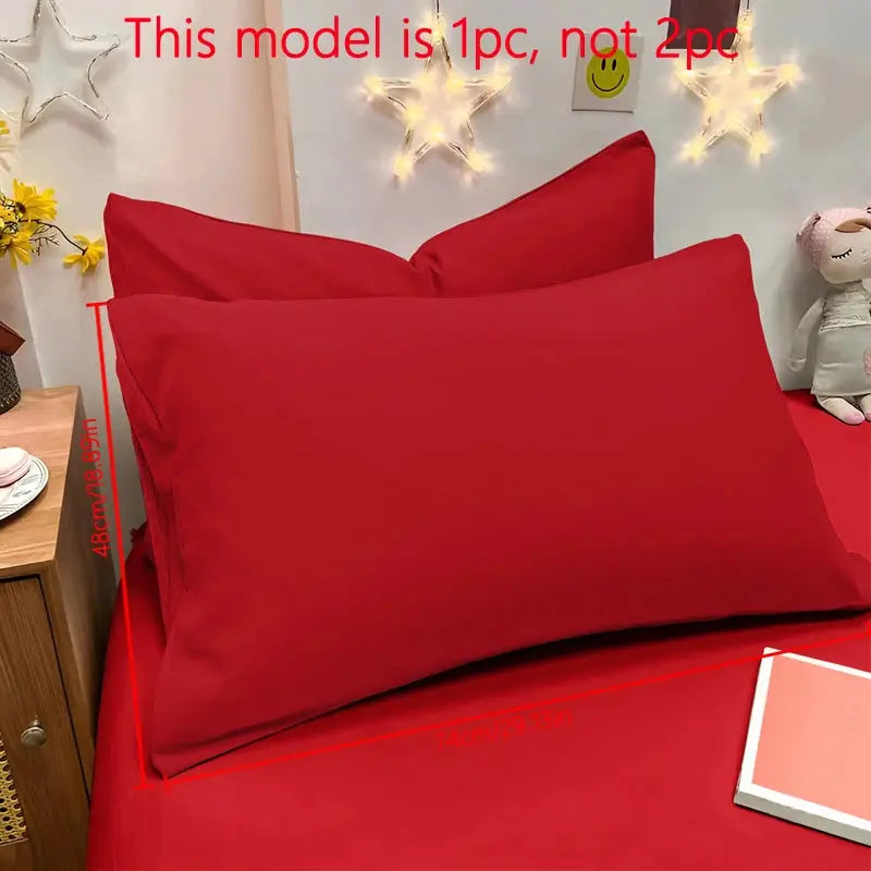 Two red matte pillowcases on a red bed with star-shaped fairy lights.