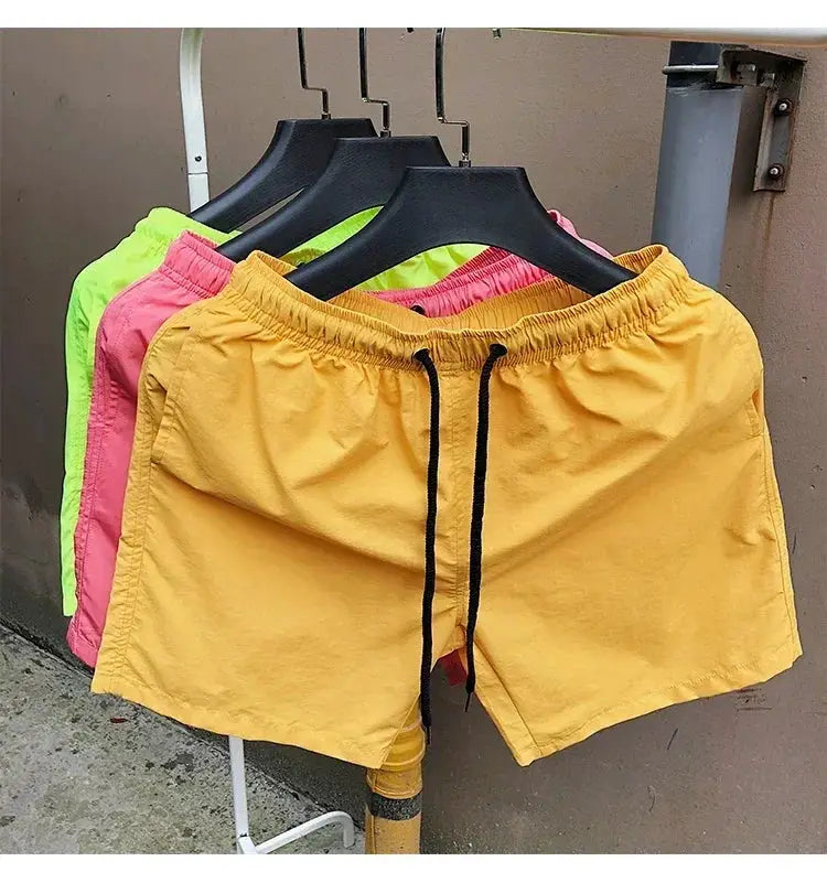 Men's swim shorts on hangers; yellow pair with black drawstrings, neon pink and lime green variants visible