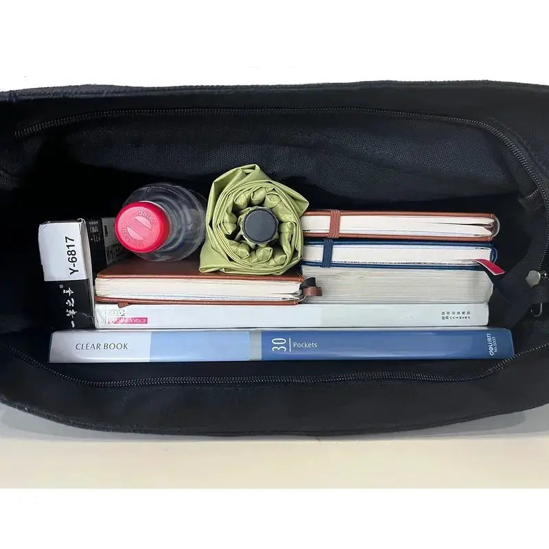 Women's black canvas messenger bag interior filled with 5+ items: books, notebooks, water bottle, umbrella.