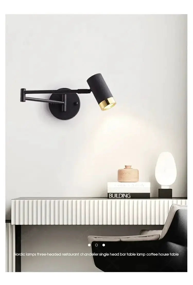 Wall lamp by Simples Market; black metal adjustable arm with gold interior shade mounted on white wall.