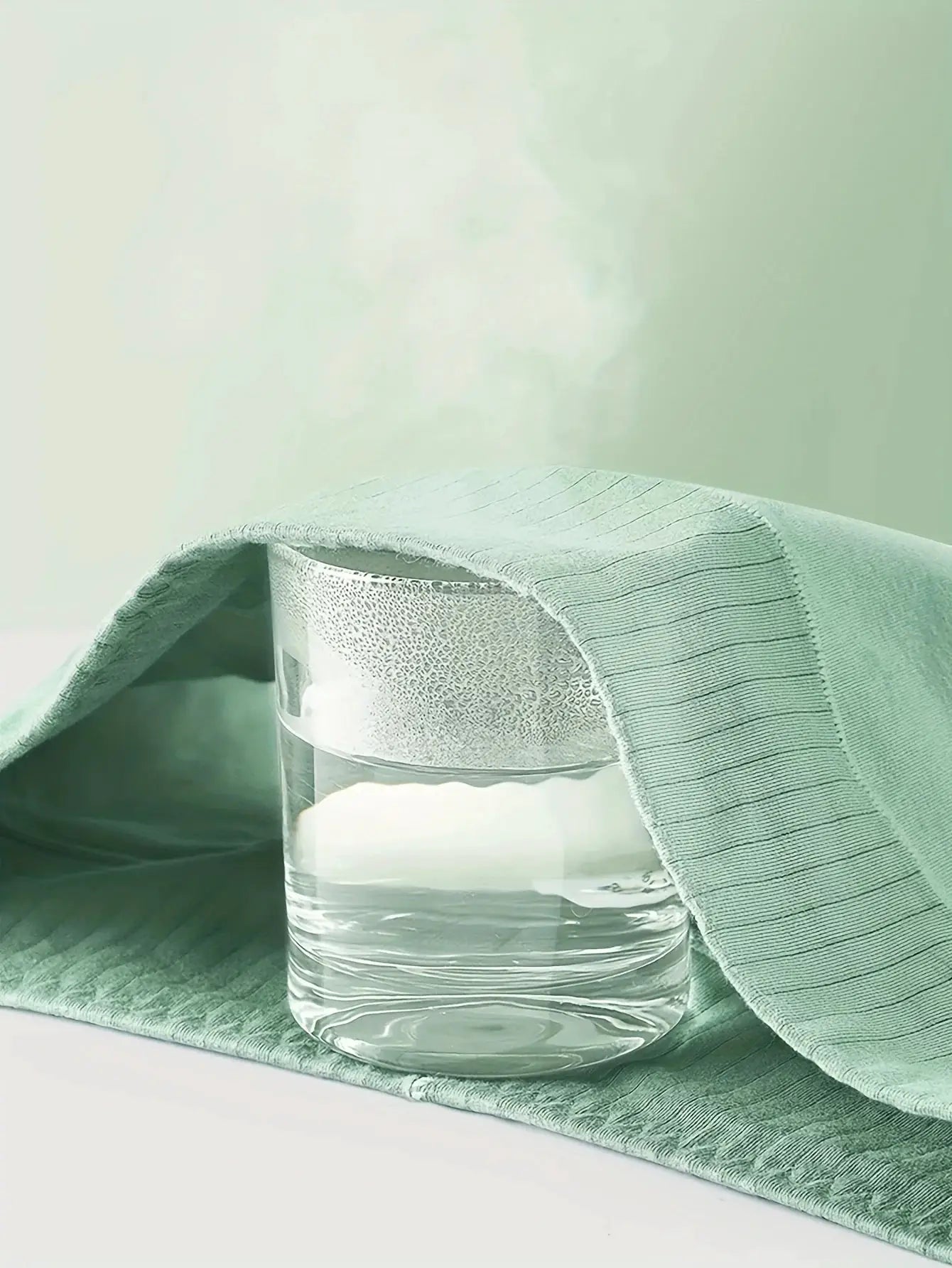 Glass of water with condensation resting on a green textured fabric.