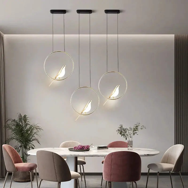 Three gold-ring magpie bird LED pendant lights hanging from ceiling above a dining table.