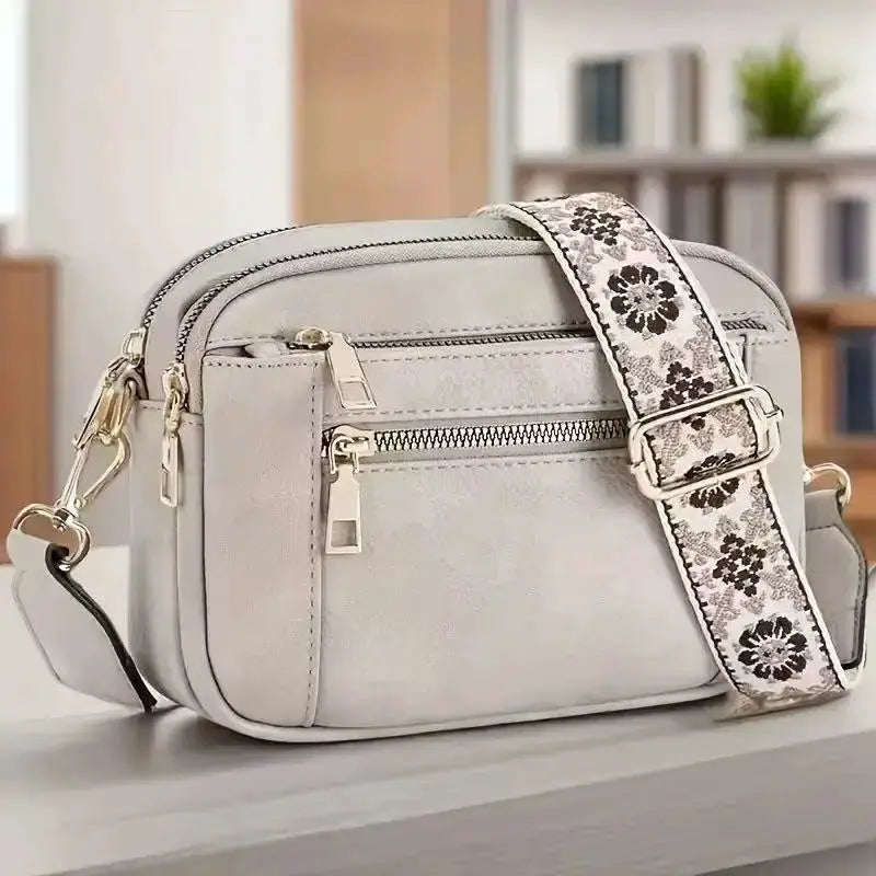 Small square crossbody bag in light gray faux leather with zip pockets and floral-pattern strap