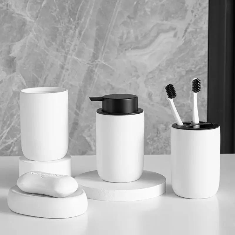 White ceramic four-piece bathroom set with mouthwash cup, pump dispenser, toothbrush holder holding two brushes, and soap dish