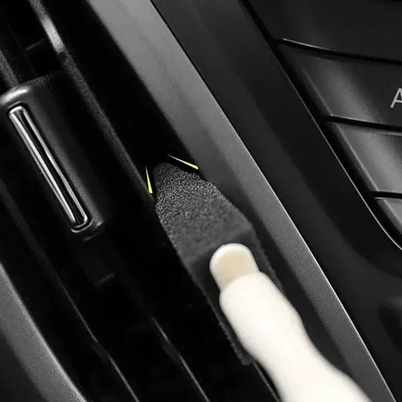 Car AC vent cleaning brush; black foam-bristle head with white handle for detailing car interior.
