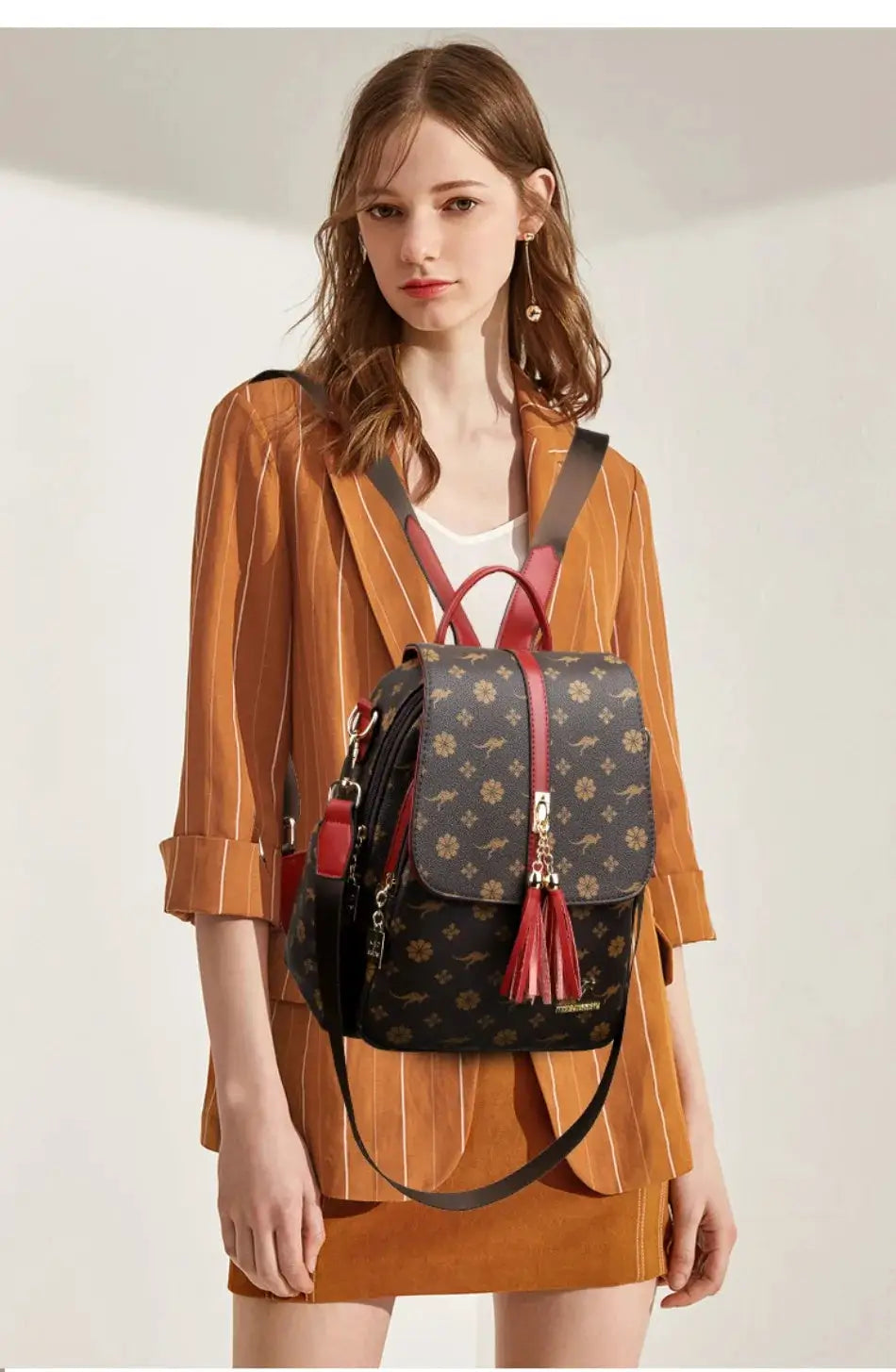 Backpack with dark floral monogram print, red tassel charm, and red trim.
