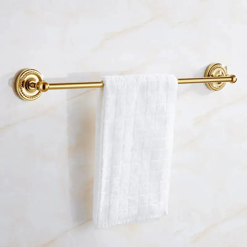 Towel bar in gold brass with ornate wall-mount brackets and white towel