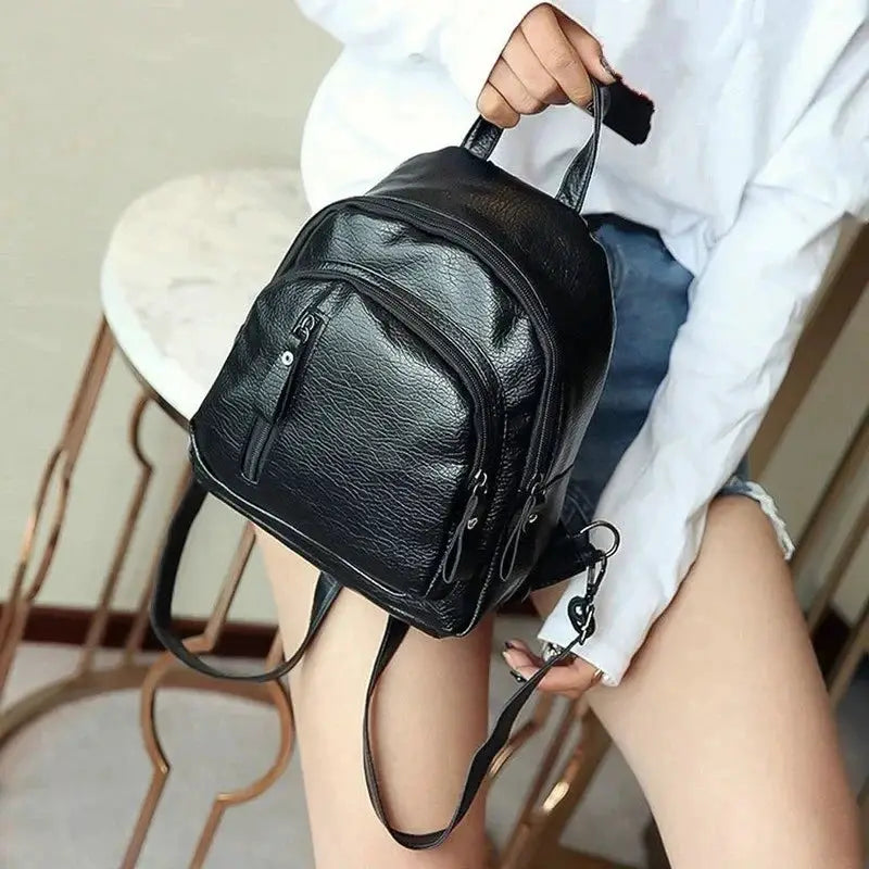 Mini black backpack with textured faux leather, top handle and multiple zip pockets.