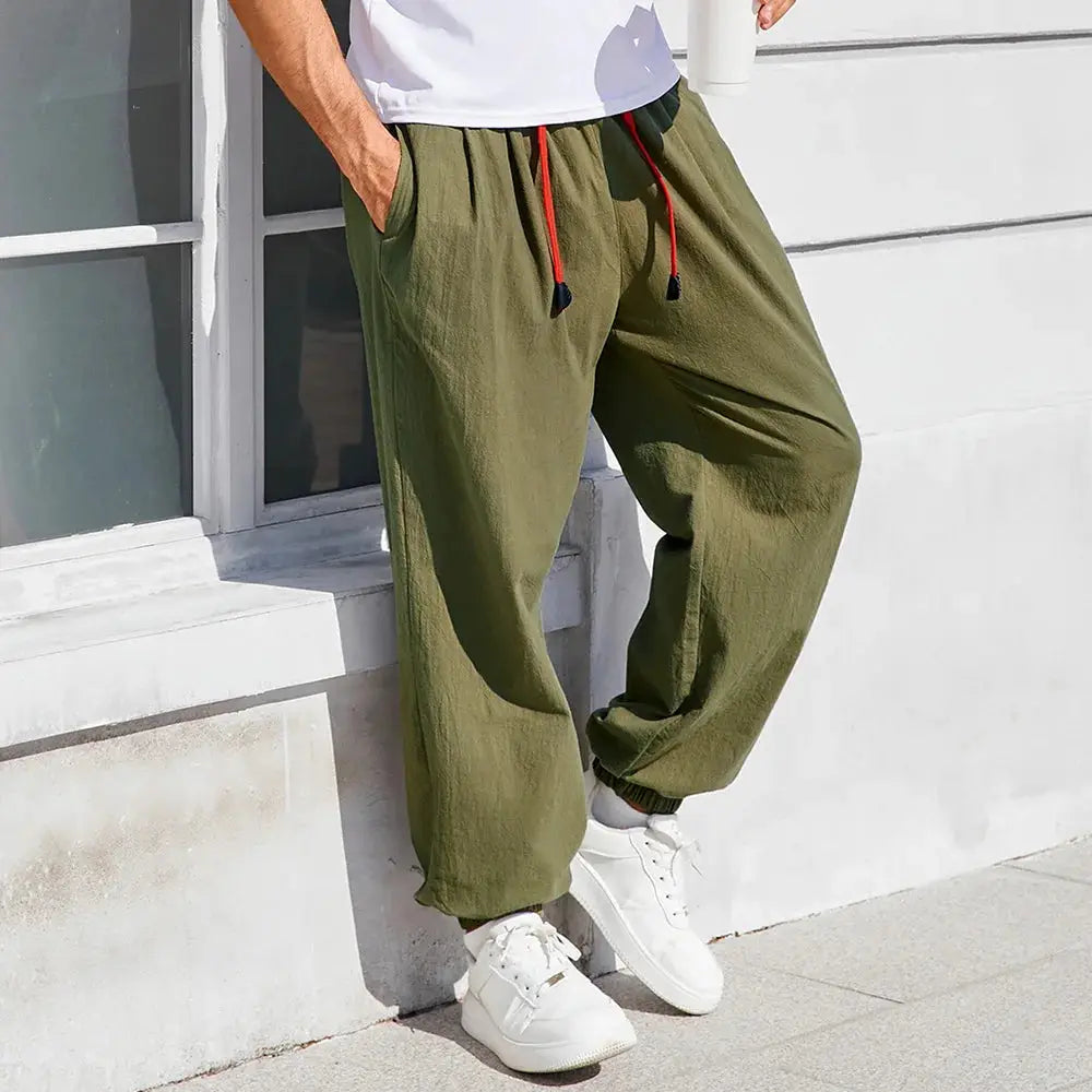 Simples Market men's harem pants in olive cotton-linen, loose-fit joggers with red drawstrings and white sneakers.