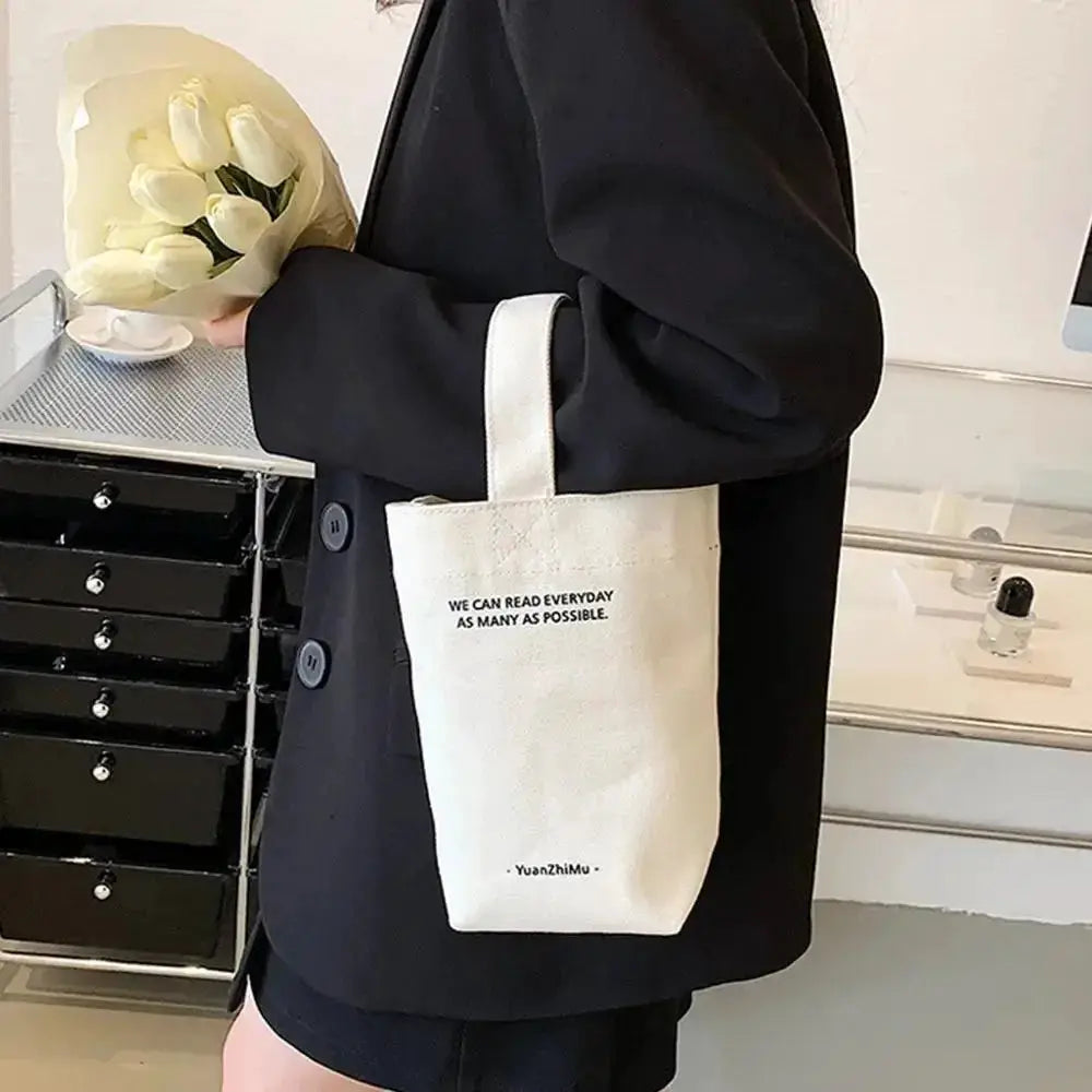 Canvas tote bag with short white handles, white fabric, printed quote, carried by a person in a black coat.
