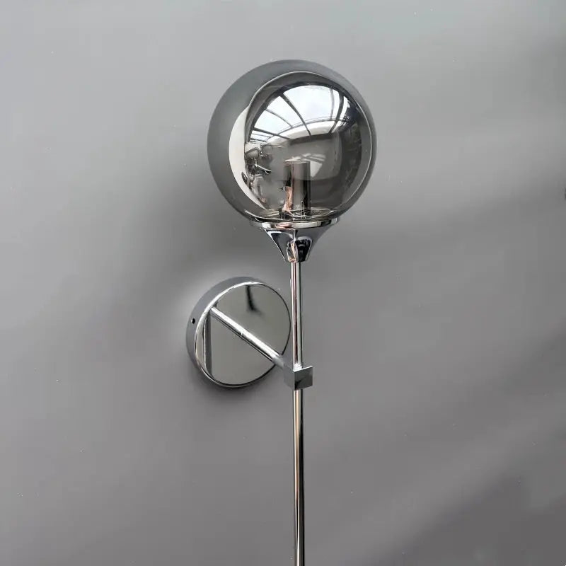 Modern glass wall lamp with a round glass globe shade atop a slim chrome stem and circular wall mount.