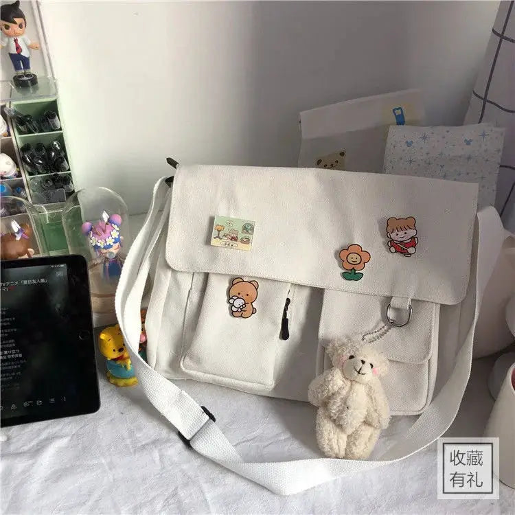 Simples Market white canvas messenger bag with cartoon patches, front pockets, and a plush bear keychain.