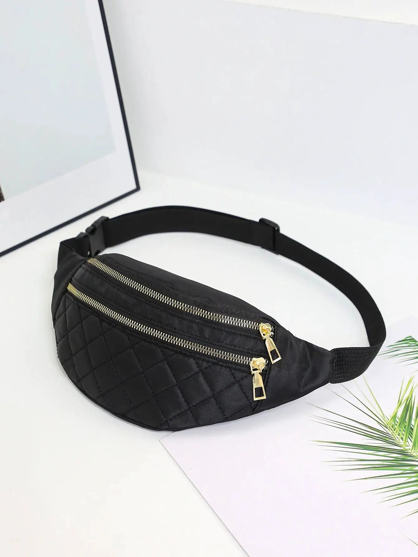 Women's black quilted waist bag with gold-tone zippers and an adjustable strap
