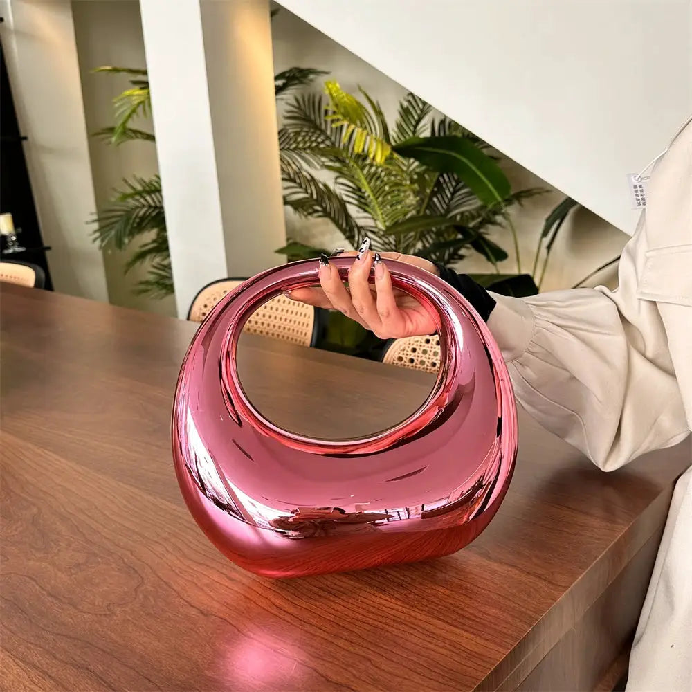 MOODS pink metallic PVC handbag with a circular handle clutch purse by Simples Market