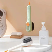 Two shoe cleaning brushes: mint-green handheld with orange button and black bristles, white brush with gray bristles.