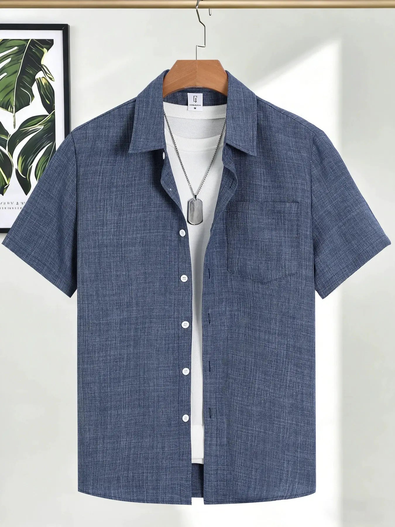 Men's blue linen short-sleeve shirt on a hanger, white tee underneath, chest pocket, with silver dog-tag necklace.