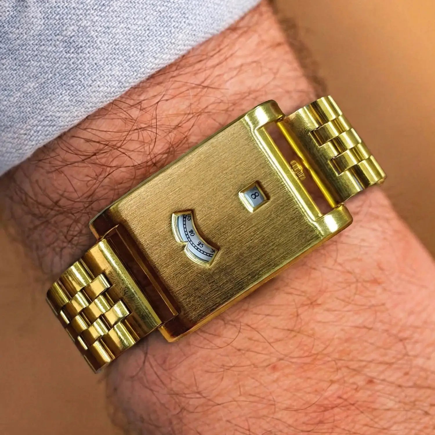 Gold square quartz watch on wrist with brushed metal band and date window