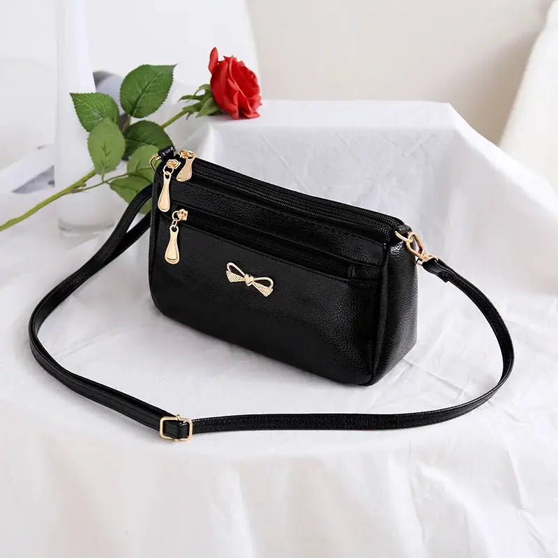 PU leather women's crossbody bag in black with gold zippers and bow emblem