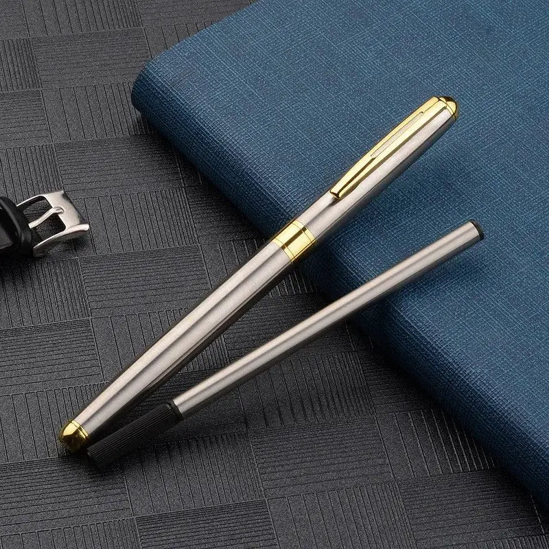 Ballpoint pen in stainless steel with gold clip and band, refillable beside a blue notebook
