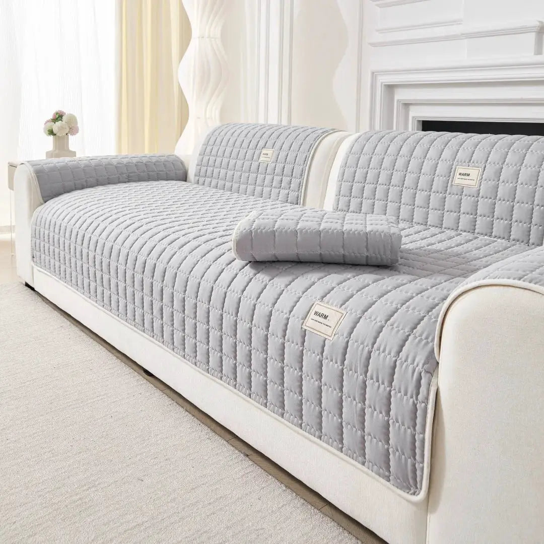 Quilted sofa cover by Simples Market in light gray on a cream sofa with a matching bolster pillow